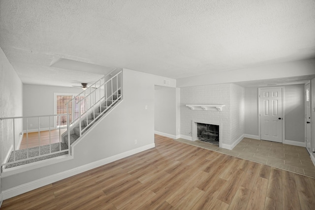 unfurnished living room featuring wood finished floors, a fireplace, stairway, a textured ceiling, and a ceiling fan