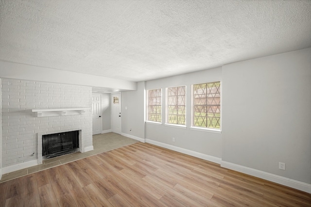 unfurnished living room featuring a textured ceiling, baseboards, a brick fireplace, and wood finished floors