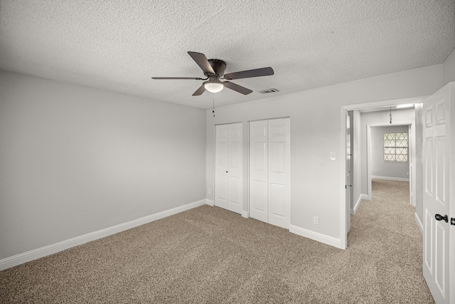 unfurnished bedroom featuring visible vents, carpet floors, multiple closets, baseboards, and a textured ceiling