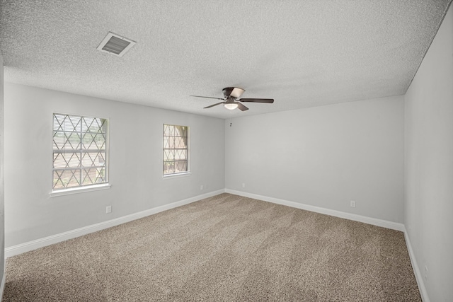 carpeted spare room with visible vents, a ceiling fan, baseboards, and a textured ceiling