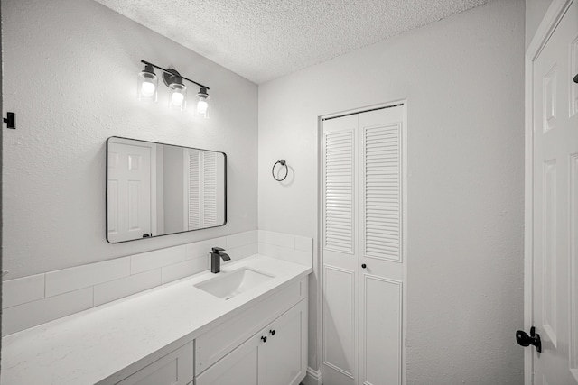 bathroom with vanity, a textured ceiling, backsplash, and a closet