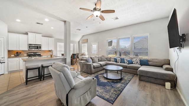 living room featuring ceiling fan, vaulted ceiling, light wood-type flooring, and visible vents