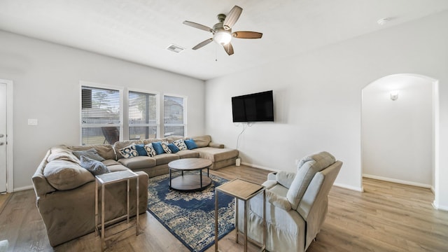 living room featuring visible vents, light wood-style floors, baseboards, ceiling fan, and arched walkways