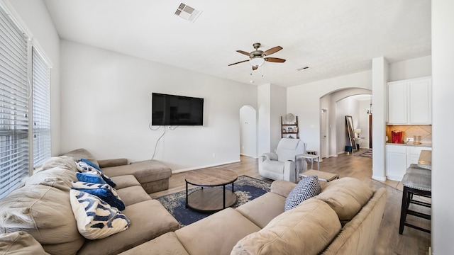 living area with visible vents, baseboards, ceiling fan, arched walkways, and light wood-style flooring
