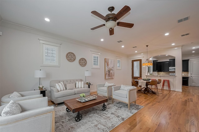 living room featuring a ceiling fan, visible vents, ornamental molding, and light wood finished floors