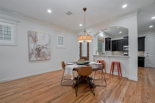 dining space featuring crown molding, light wood-style floors, arched walkways, recessed lighting, and visible vents