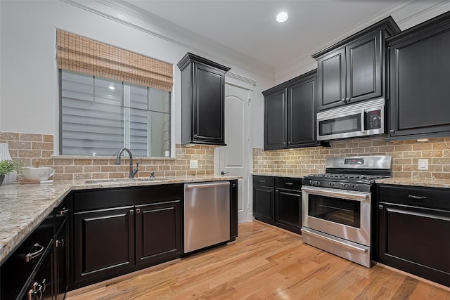 kitchen featuring appliances with stainless steel finishes, dark cabinets, a sink, light stone counters, and light wood-style floors