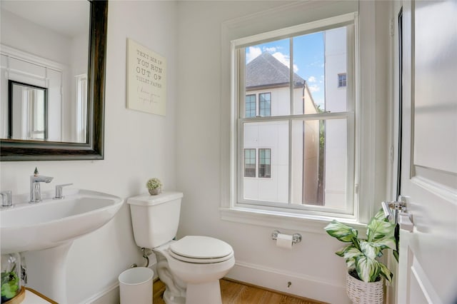 half bath with toilet, baseboards, a sink, and wood finished floors