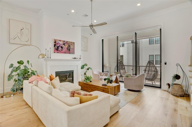living area featuring a ceiling fan, visible vents, crown molding, wood finished floors, and a glass covered fireplace
