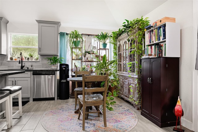 interior space with dark countertops, a sink, light wood-style floors, backsplash, and stainless steel dishwasher