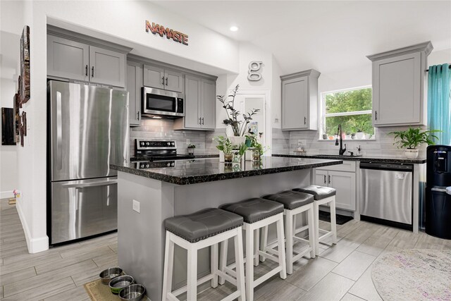 kitchen with a sink, gray cabinets, a breakfast bar area, and stainless steel appliances
