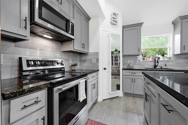 kitchen featuring a sink, appliances with stainless steel finishes, gray cabinets, and dark stone countertops
