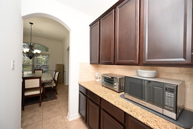 kitchen featuring backsplash, dark brown cabinets, an inviting chandelier, and light stone counters