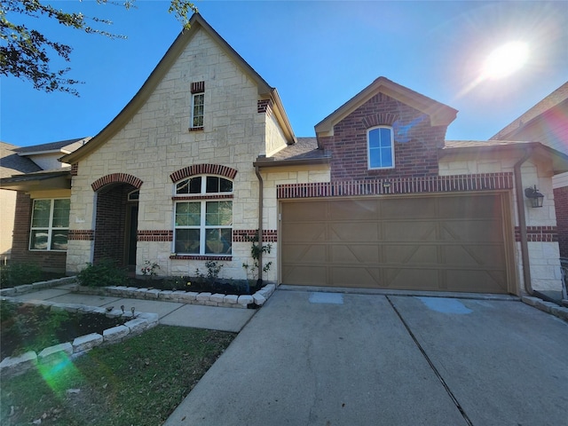view of front facade featuring an attached garage, brick siding, driveway, and stone siding