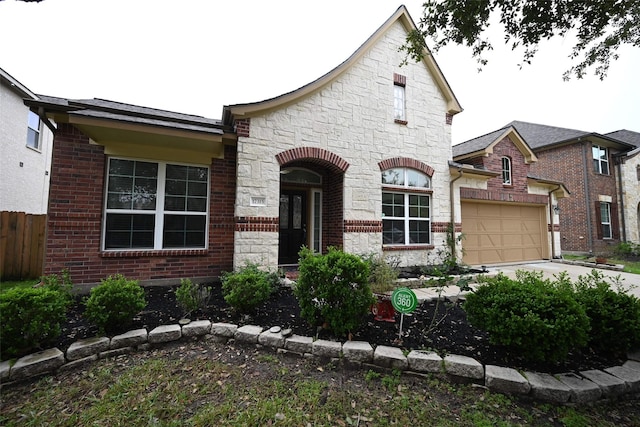 french country home with an attached garage, fence, driveway, and stone siding