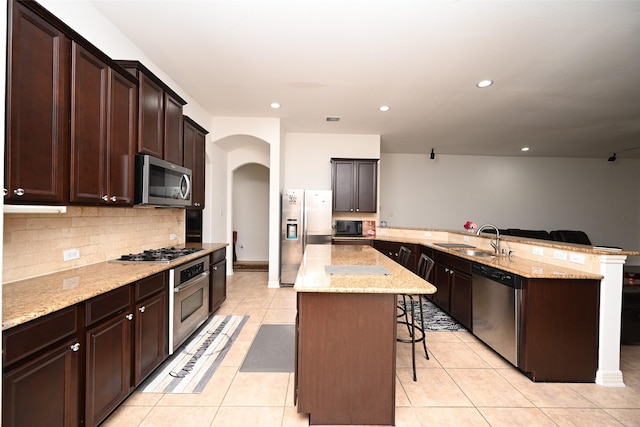 kitchen featuring a peninsula, a kitchen bar, arched walkways, a sink, and appliances with stainless steel finishes