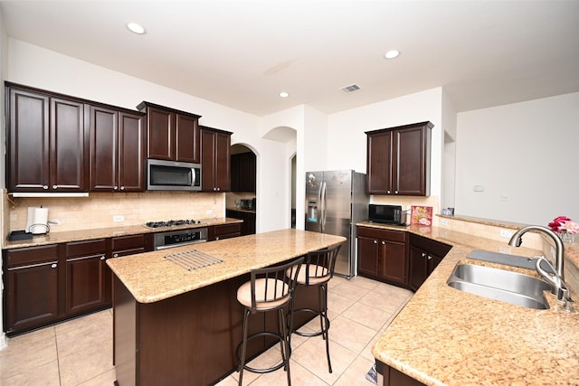kitchen featuring a sink, arched walkways, a center island, stainless steel appliances, and light tile patterned floors