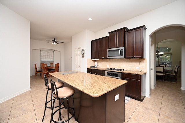 kitchen with ceiling fan, decorative backsplash, a kitchen bar, appliances with stainless steel finishes, and light tile patterned floors