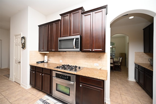 kitchen featuring light stone countertops, stainless steel appliances, light tile patterned flooring, and backsplash