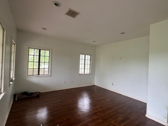 empty room featuring plenty of natural light, baseboards, dark wood-style floors, and visible vents