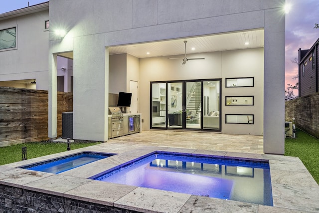 rear view of house with fence, an outdoor kitchen, stucco siding, an in ground hot tub, and a patio area