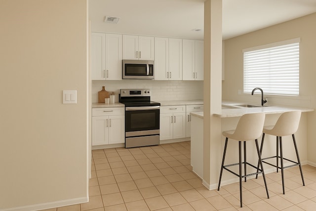kitchen with a sink, a kitchen breakfast bar, stainless steel appliances, light tile patterned floors, and visible vents