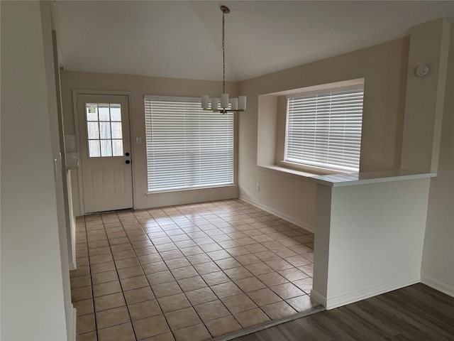 unfurnished dining area featuring baseboards, lofted ceiling, tile patterned floors, and a chandelier