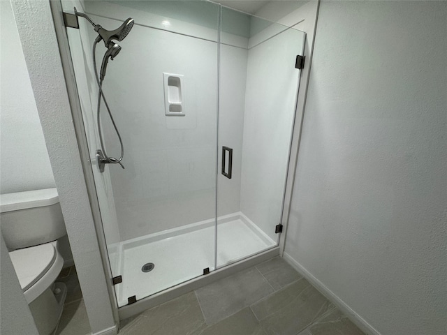 bathroom with toilet, a textured wall, baseboards, and a stall shower