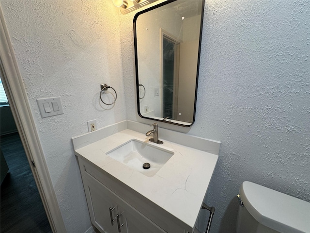 half bath featuring vanity, a textured wall, and toilet
