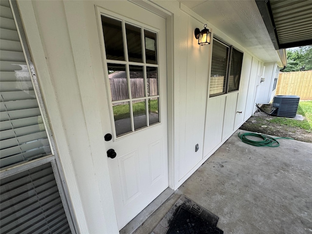 doorway to property with central air condition unit, fence, and board and batten siding