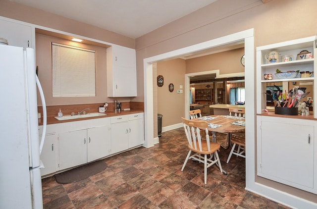 kitchen featuring freestanding refrigerator, stone finish floor, light countertops, white cabinets, and a sink