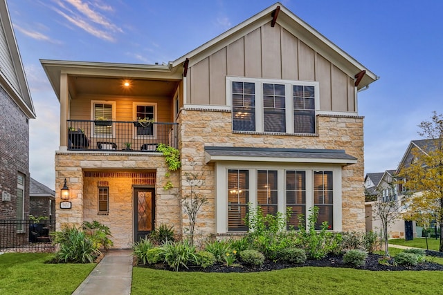 modern home with a front yard, board and batten siding, a balcony, and stone siding