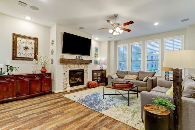 living area with ceiling fan, visible vents, wood finished floors, baseboards, and a glass covered fireplace