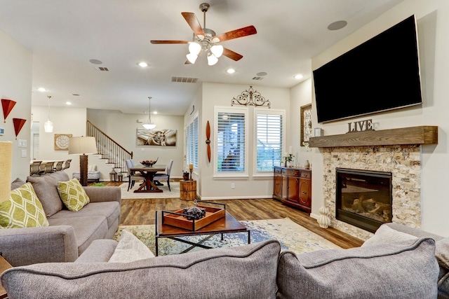 living room with ceiling fan, a glass covered fireplace, stairs, wood finished floors, and visible vents