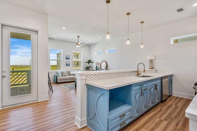 kitchen featuring plenty of natural light, stainless steel dishwasher, light wood-type flooring, a sink, and a peninsula