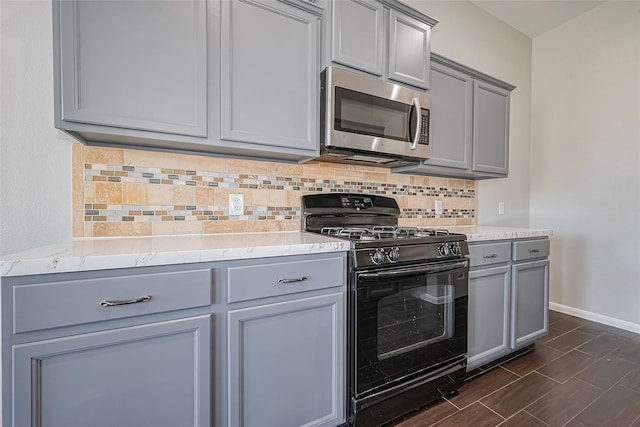 kitchen featuring baseboards, stainless steel microwave, gray cabinetry, and black gas range oven