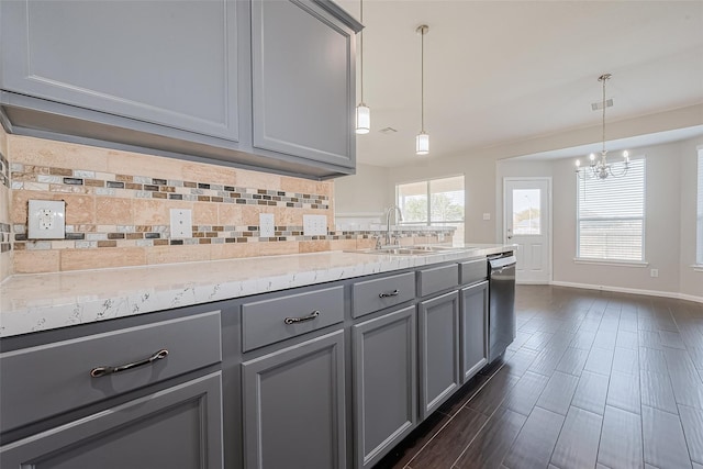kitchen featuring a notable chandelier, a sink, backsplash, stainless steel dishwasher, and gray cabinetry