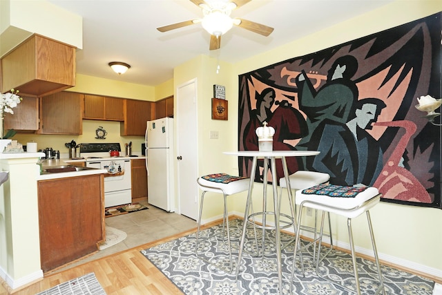kitchen featuring white appliances, light countertops, brown cabinetry, light wood-style flooring, and a ceiling fan
