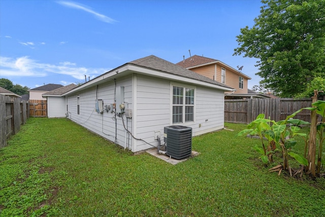 rear view of house with roof with shingles, a fenced backyard, a yard, and central AC