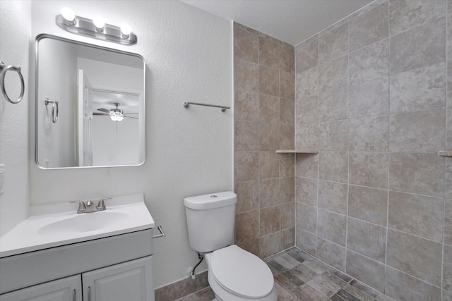 bathroom with vanity, a ceiling fan, a tile shower, and toilet