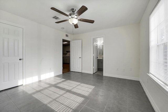 unfurnished bedroom with dark tile patterned flooring, baseboards, ensuite bath, and visible vents