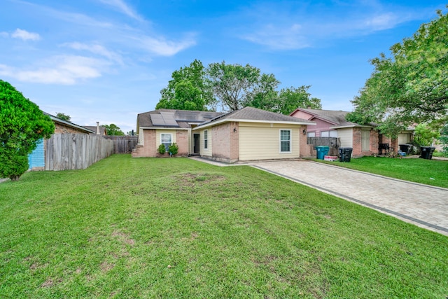 single story home featuring a front lawn, fence, decorative driveway, brick siding, and solar panels