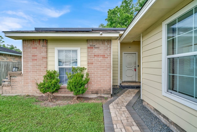 doorway to property with fence, a lawn, and brick siding