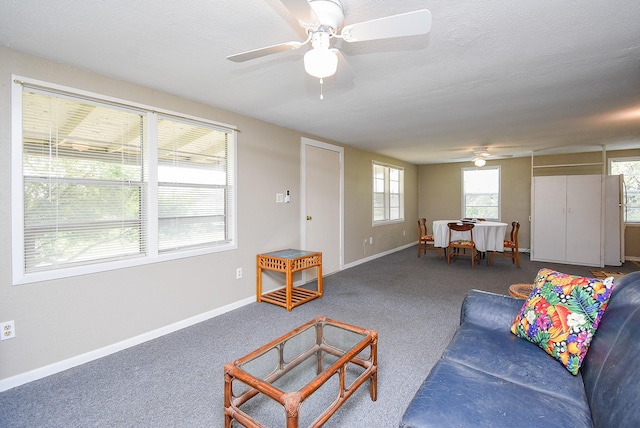 carpeted living area with ceiling fan and baseboards