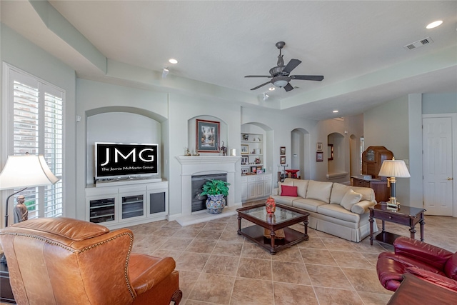 living area featuring visible vents, built in features, recessed lighting, a fireplace with raised hearth, and a ceiling fan