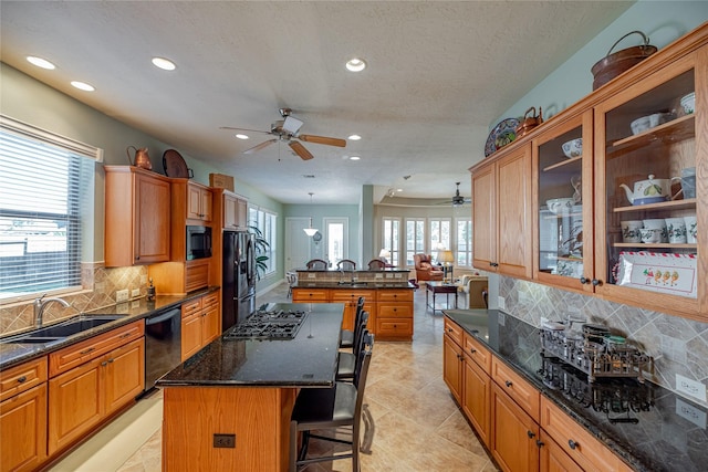 kitchen with a ceiling fan, a kitchen bar, a center island, a sink, and black appliances