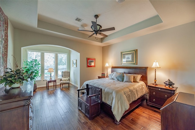 bedroom with visible vents, arched walkways, baseboards, wood-type flooring, and a tray ceiling