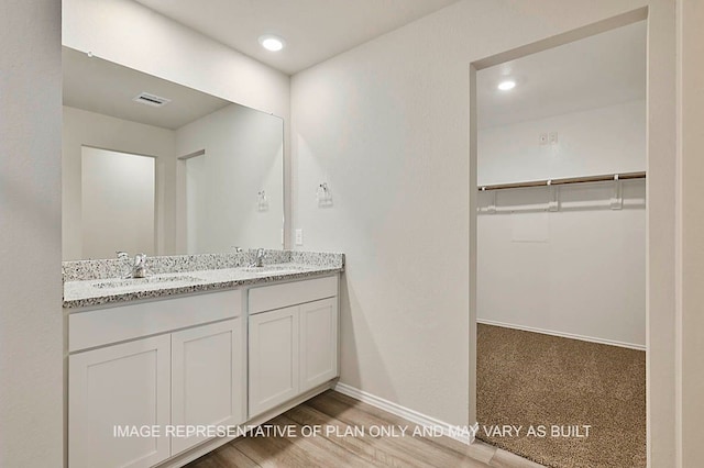 bathroom featuring double vanity, visible vents, a sink, baseboards, and a spacious closet