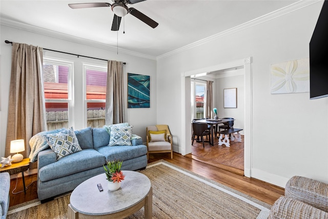 living area featuring baseboards, ceiling fan, ornamental molding, and wood finished floors