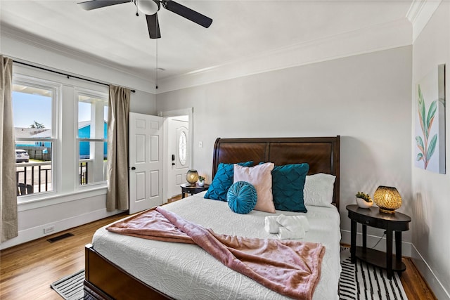 bedroom with ceiling fan, baseboards, wood finished floors, visible vents, and ornamental molding